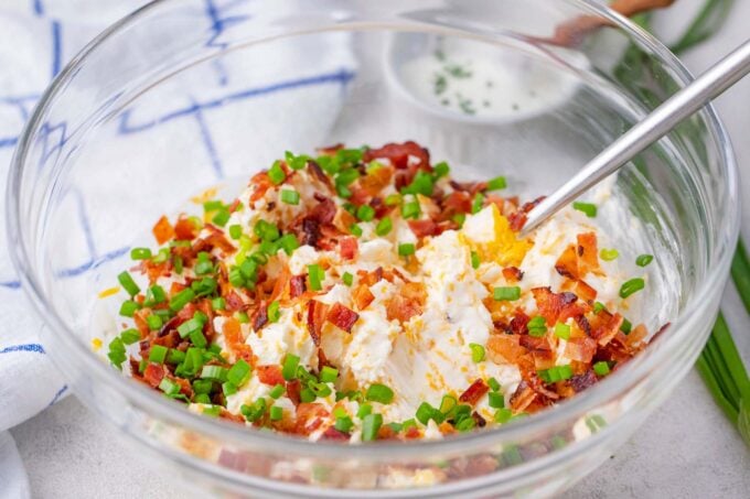 Cream cheese, bacon, cheddar and green onions on a bowl.