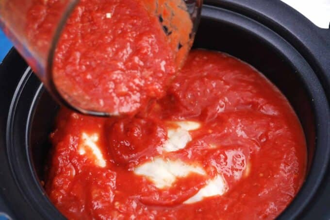 pouring tomato sauce on top of cabbage rolls in a slow cooker